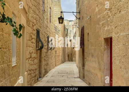 Mdina, Malte allée vide le long de maisons en pierre dans la ville médiévale historique de Silent pavée de dalles de pierre et de murs de calcaire avec lanternes suspendues. Banque D'Images