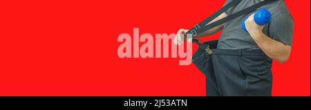 L'homme tire son grand pantalon à sa taille et tient une haltère. Montre comment il a perdu du poids. Banque D'Images