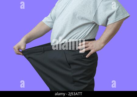 L'homme tire sur son grand pantalon à la taille. Montre comment il a perdu du poids. Banque D'Images