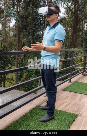Photo verticale d'un homme utilisant des lunettes de réalité virtuelle sur une terrasse dans un environnement naturel au milieu des arbres Banque D'Images