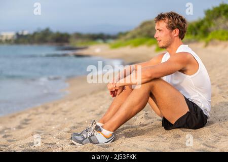 FIT jeune homme sain et actif style de vie se reposant sur la plage après l'entraînement. Portrait d'athlète masculin caucasien assis en plein air reposant Banque D'Images