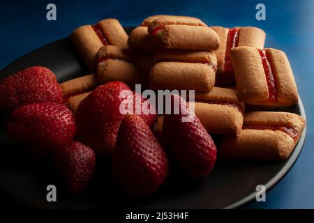 Une pile de barres de biscuits Strawberry sur une plaque noire au-dessus d'une table bleu foncé et d'une macro-photographie d'arrière-plan noir Banque D'Images