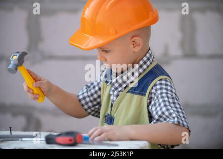 Portrait de petit constructeur en casques avec instruments pour la rénovation sur la construction. Garçon de créateur, enfant de menuisier avec ensemble d'outils de constructeur. Enfants Banque D'Images