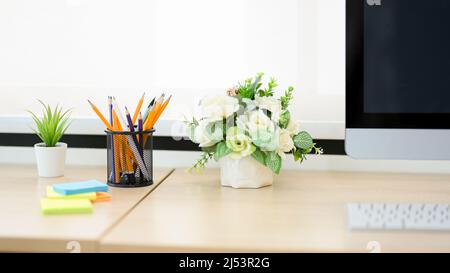 Gros plan, bureau féminin avec ordinateur, clavier, papeterie, notes adhésives et vase avec fleurs roses. Banque D'Images