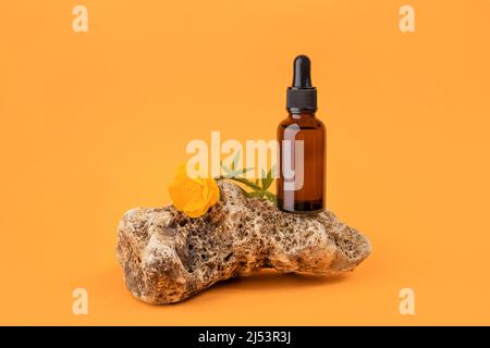 Sérum ou huile essentielle dans un flacon compte-gouttes en verre brun sur pierre et fleurs sur fond orange. Natural Organic Spa concept vue de face. Banque D'Images