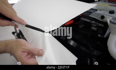 Film de protection de voiture blanc. Habillage automatique. Un travailleur professionnel installe une protection contre la peinture. Mise à niveau de la voiture avec un film de protection continu. Banque D'Images