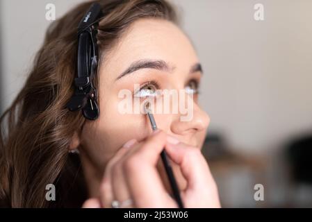 Maquilleuse application de l'ombre oculaire à la paupière inférieure d'une fille avec un pinceau. Photo de haute qualité Banque D'Images