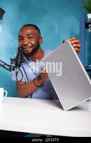 Portrait d'un influenceur afro-américain accueillant des cadeaux en direct pour la célèbre marque d'ordinateur portable parlant dans le microphone. Concours de création de contenu pour l'enregistrement de balados vidéo sur les réseaux sociaux. Banque D'Images