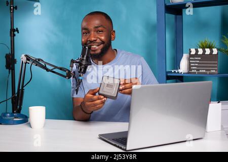 Enregistrement de vlogger souriant pour le site Web assis à un bureau avec ordinateur portable dans le studio de vlogging avec configuration professionnelle en direct. Influenceur accueillant une présentation de produit en ligne tout en parlant dans le microphone. Banque D'Images