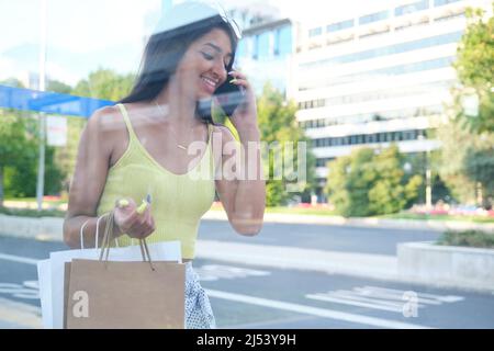 Jeune femme latine parlant au téléphone en attendant le bus à un arrêt de bus. Banque D'Images