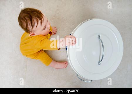 Bébé garçon ouvre une poubelle avec les déchets ménagers. Problèmes de sécurité des enfants dans la chambre d'accueil, petit enfant Banque D'Images