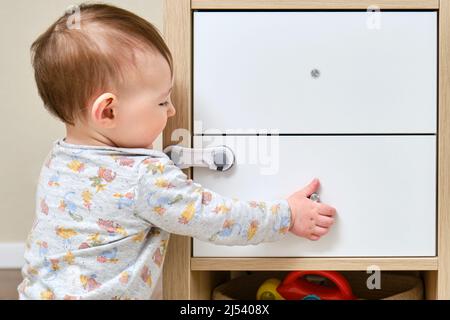 Bébé garçon se déporte d'un tiroir de cabinet avec sa main. L'enfant tient la poignée de la porte de l'armoire, petit enfant Banque D'Images