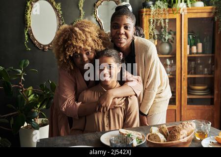 Portrait de trois sœurs embrassant et souriant à la caméra tout en étant assis à table pendant le dîner en famille Banque D'Images