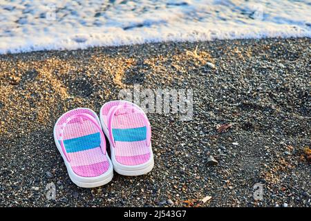 Pantoufles roses pour enfants sur une plage de galets Banque D'Images