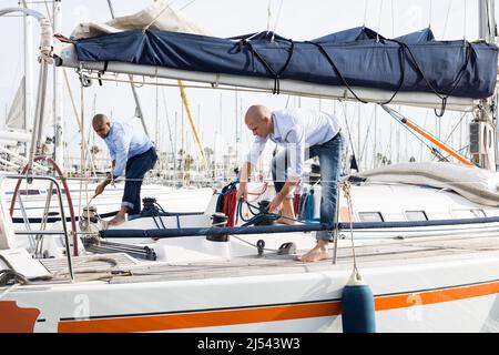 Deux jeunes hommes en chemises bleues arrange le yacht privé de voile dans le port maritime Banque D'Images