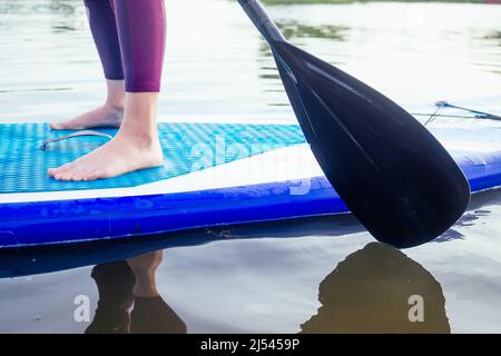 Montez le paddle-board sur un lac de mer calme, gros plan des jambes et des éclaboussures d'eau Banque D'Images