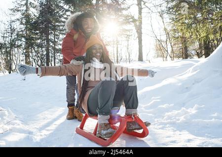 Joyeux homme et femme afro-américain amoureux de s'amuser les jours d'hiver en traîneau dans les montagnes locales Banque D'Images