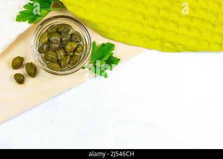 Vue de dessus de petits câpres vertes cueils fruits dans un bol en verre trempée sur fond de bois clair dans la cuisine avec un espace pour copier. Banque D'Images