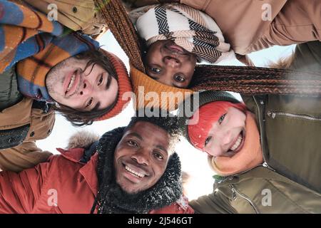 D'en dessous de la vue de jeunes Afro-américains et caucasiens amis passer une journée d'hiver enneigée ensemble souriant à la caméra Banque D'Images