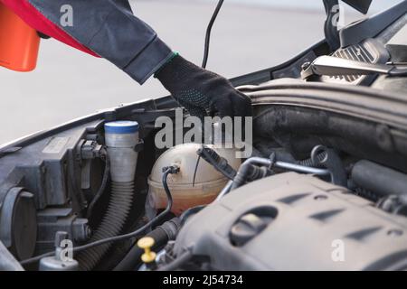 Auto Mechanic dévisse le bouchon du vase d'expansion pour verser l'antigel dans l'atelier d'entretien automobile Banque D'Images