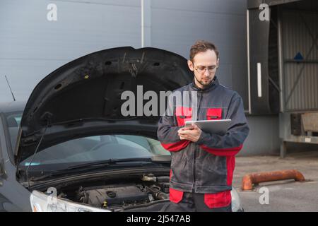 Mécanicien caucasien en uniforme utilisant un PC tablette au poste de réparation de voiture. Entretien de la voiture Banque D'Images