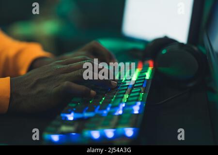 Gros plan de mains afro-américaines dactylographiées sur un clavier d'ordinateur de bureau lumineux et coloré tout en étant assis en studio ou dans une caffe Internet à l'intérieur. . Photo de haute qualité Banque D'Images