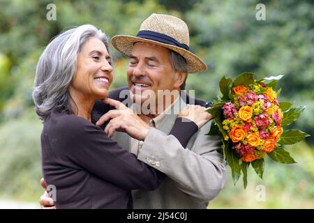 couple âgé dans le parc, l'homme la déchire avec amour après lui avoir donné un bouquet de fleurs Banque D'Images