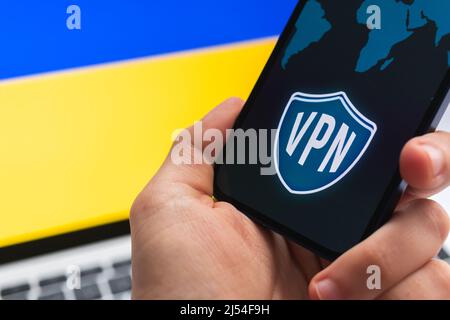 VPN en Ukraine. Concept Internet sécurisé et sûr. Confidentialité. Main avec le téléphone mobile et l'application VPN. Drapeau et ordinateur portable sur la photo d'arrière-plan Banque D'Images