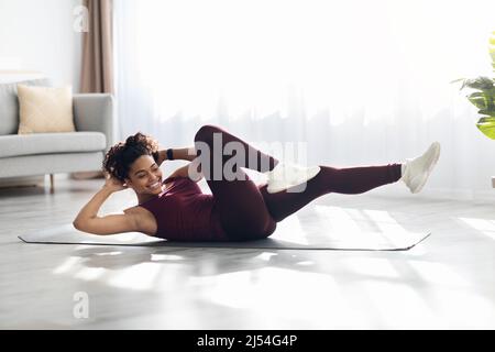 Femme afro-américaine athlétique s'exerçant sur un tapis de fitness à la maison Banque D'Images