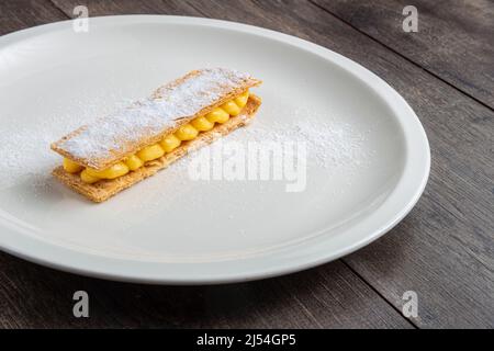 Pâte feuilletée pantxineta avec crème au citron et sucre glace sur une assiette blanche sur un fond rustique en bois. Dessert typique du pays basque espagnol Banque D'Images