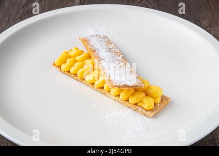 Pâte feuilletée pantxineta avec crème au citron et sucre glace sur une assiette blanche sur un fond rustique en bois. Dessert typique du pays basque espagnol Banque D'Images