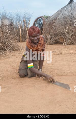 Les Nyangatom (Bumi) une femme sur ses genoux et gratter le sol avec une machette, vallée de la rivière Omo, en Ethiopie Banque D'Images