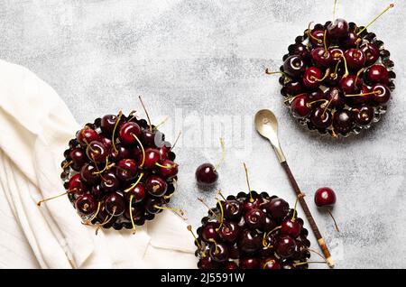 Cerises dans des mini casseroles avec une cuillère et une serviette blanche, sur un fond gris avec espace copie. Banque D'Images