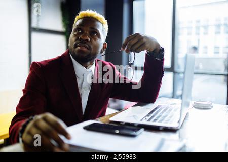 afro-américain assis au bureau en tapant une note de message sur le téléphone près d'un ordinateur portable Banque D'Images