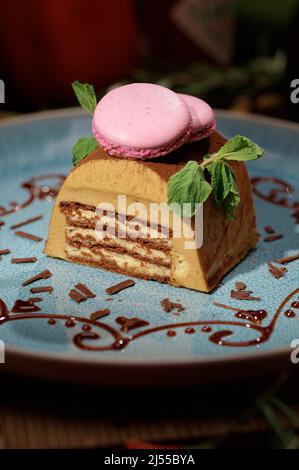 Délicieux gâteau au chocolat sur l'assiette, décoré de feuilles de menthe fraîche et de macaron rose. Banque D'Images