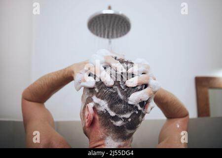 Vue arrière de l'homme tout en lavant les cheveux dans la douche dans la salle de bains. Mouiller les cheveux avec de la mousse de shampooing. Banque D'Images