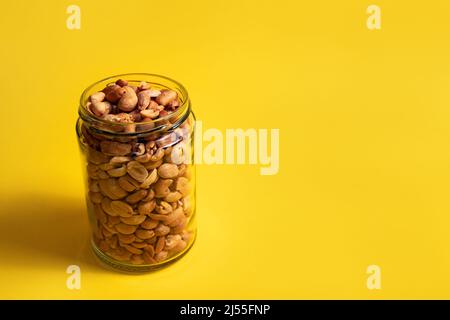 Arachides dans un pot en verre sur fond jaune Banque D'Images