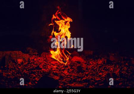 Flamme rouge de feu qui s'élève de la pierre recouverte de feuilles d'automne. Banque D'Images