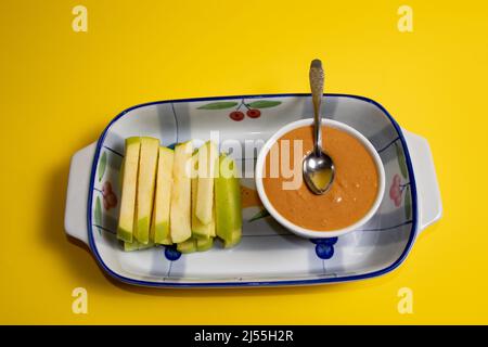 Tranches de pomme verte et beurre d'arachide dans une tasse. Arrière-plan jaune. Banque D'Images