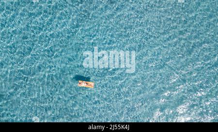 Femme flottant sur le matelas gonflable de lilo sur la surface bleue transparente de l'eau en été vacances loisirs activité. Les touristes féminins se détendent Banque D'Images