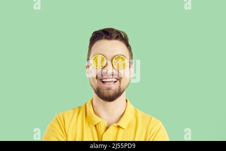 Homme positif gai dans des verres d'été en forme de tranches d'orange sur fond vert clair. Banque D'Images