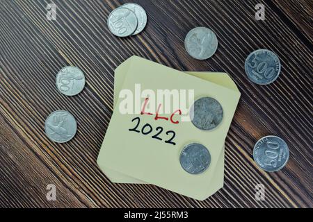 LLC 2022 écrire sur les notes adhésives et la monnaie indonésienne isolée sur la table en bois. Banque D'Images