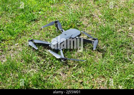 Un mini-drone s'est déployé sur une herbe avant le décollage. Un petit drone survole le parc pour prendre des vidéos et des photos. Livraison d'air à distance et Spy. Banque D'Images