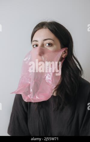 Auto-isolement en cas de pandémie. Portrait artistique flou. Covid-19 anxiété. Femme effeurée dans un masque facial protecteur sac cellophane en rouge bleu néon sur le wrink Banque D'Images