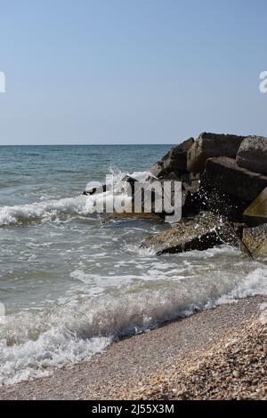 Les vagues de la mer turquoise se brisent sur les rochers côtiers et une mousse blanche dense se forme. Ciel bleu clair. Vagues blanches se brisant sur la plage de sable fin thr Banque D'Images