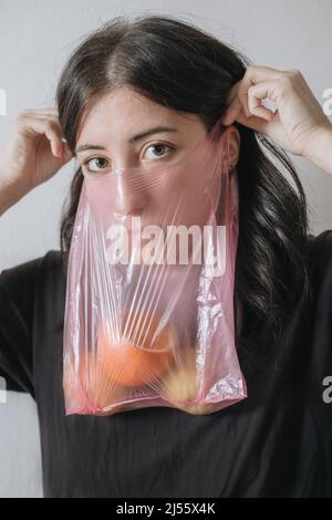 Auto-isolement en cas de pandémie. Portrait artistique flou. Covid-19 anxiété. Femme effeurée dans un masque facial protecteur sac cellophane en rouge bleu néon sur le wrink Banque D'Images