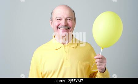 Bonne photo de vacances. Homme souriant senior avec ballon jaune et hélium en main Banque D'Images