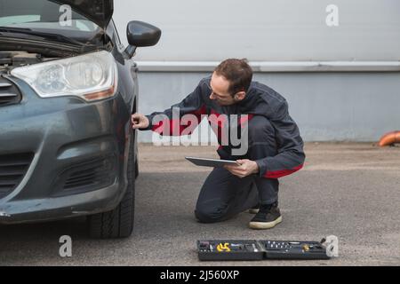 Mécanicien avec tablette PC électronique contrôlant les roues et les pneus pendant le travail dans le centre de réparation de voiture Banque D'Images