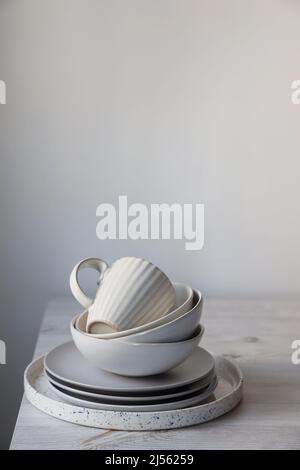 Une pyramide de bols blancs, assiettes et tasses de différentes tailles et couleurs sur une table beige dans la cuisine.Style scandinave.Place pour votre texte.Copier Banque D'Images