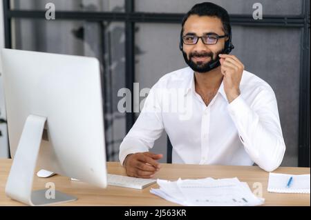 Portrait d'un bel homme indien intelligent et positif portant des lunettes et un casque, expert de la hotline, opérateur de centre d'appel, regarde directement l'appareil photo, souriant amical. Concept de service d'assistance Banque D'Images